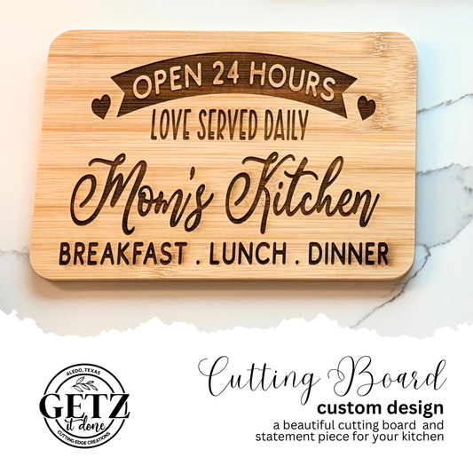 A wooden cutting board featuring the text: Open 24 Hours, Love Served Daily, Moms Kitchen, Breakfast, Lunch, Dinner with heart accents. Below, a logo reads Getz it done with additional text Cutting Board, custom design, a beautiful cutting board and statement piece for your kitchen.