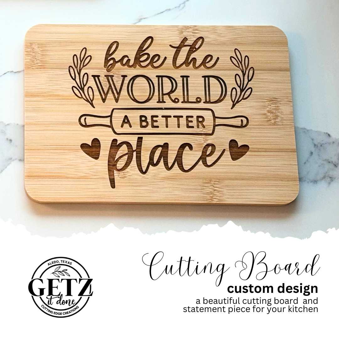 A wooden cutting board with the phrase Bake the World a Better Place engraved in elegant script, surrounded by decorative branches and a rolling pin. Below, a circular logo reads Getz It Done, Laredo, Texas, Cutting Edge Creations. Text describes it as a custom design.