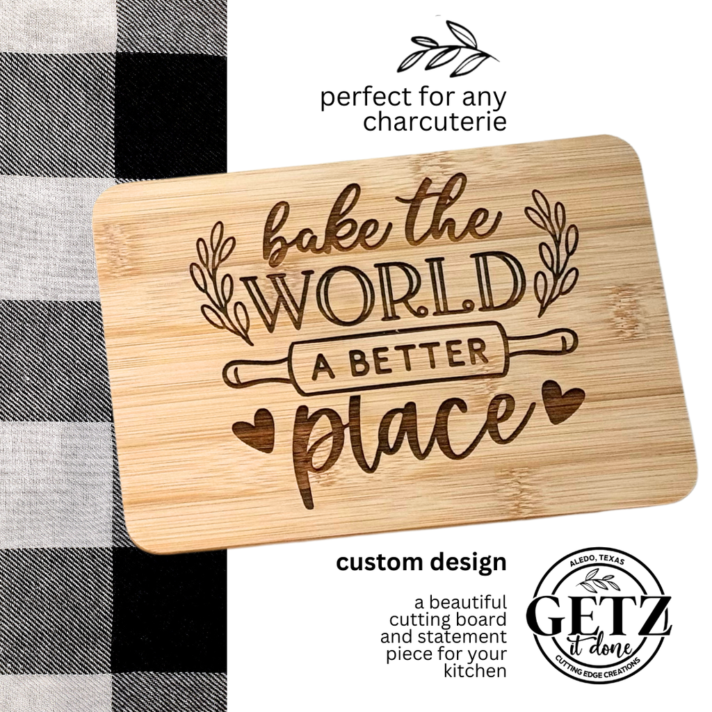 A wooden cutting board with decorative text reading Bake the World a Better Place above a rolling pin illustration. Surrounding the text are small heart and leaf designs. Its set against a black and white checkered fabric, with branding and custom design text in the corners.
