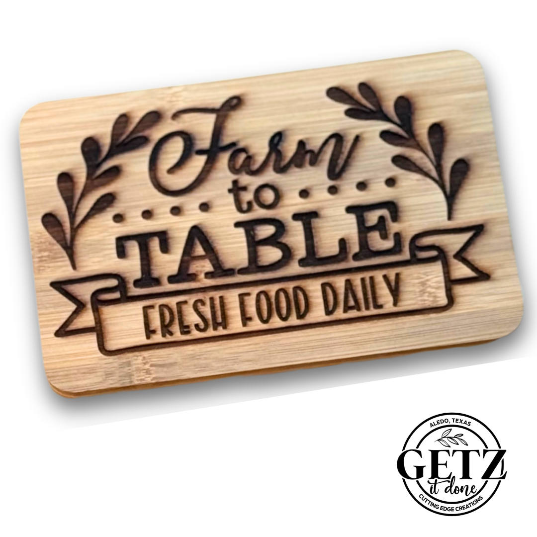 Wooden cutting board engraved with the text Farm to Table, Fresh Food Daily surrounded by decorative leaves. The bottom right corner displays a circular logo with the text Getz it done and Alto, Texas.