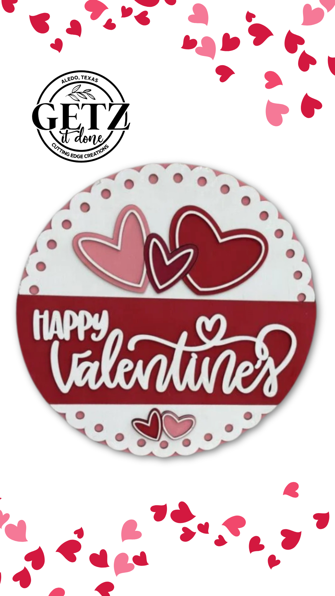 A round Valentines Day sign with Happy Valentines in white cursive on a red background. Two large overlapping hearts, one pink and one red, rest above the text. Small pink and red hearts scatter around the sign. The background features a logo and more heart decorations.