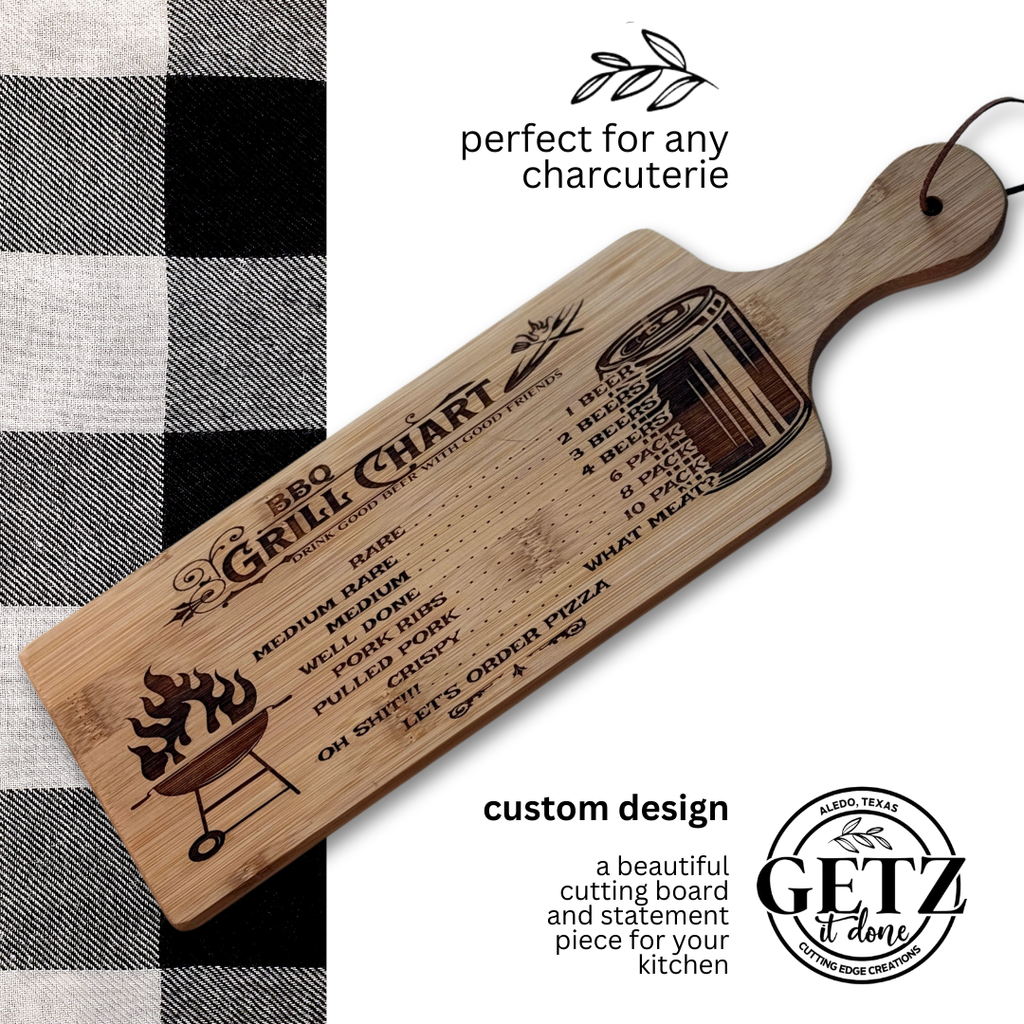 A wooden cutting board with a BBQ Grill Chart engraved, showing meat doneness levels from rare to well done. A grilling illustration and perfect for any charcuterie text are visible. The board has a handle, a leather strap, and rests on a black-and-white checkered cloth.