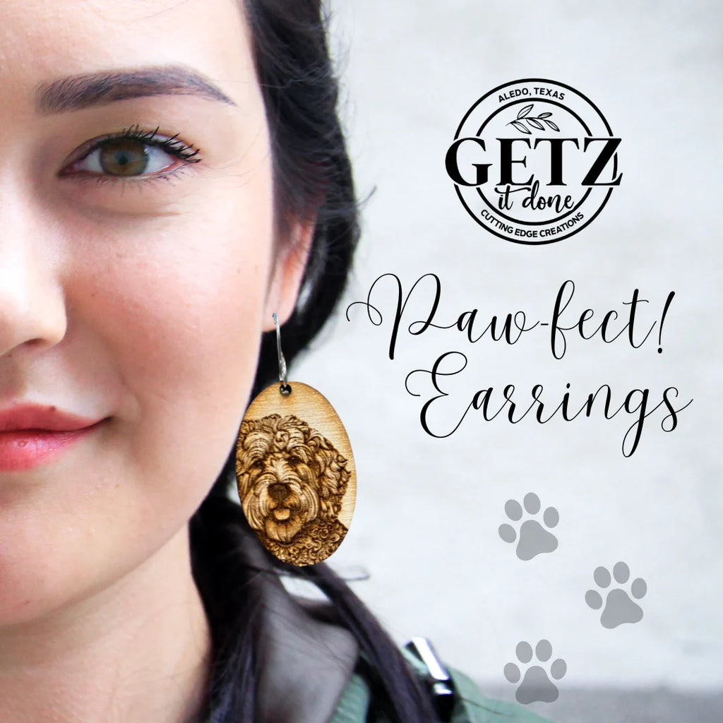 Close-up of a womans face showing a large earring with a carved dog design. Text reads GETZ it done, Paw-fect! Earrings, with paw print graphics. The background is blurred, focusing on the earring and accompanying text on the right side.