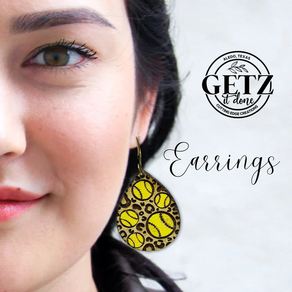 Close-up of a person wearing a teardrop-shaped earring featuring a leopard print design with yellow softball patterns. The background text reads GETZ it done with Earrings. The backdrop is light and minimalist, highlighting the earrings unique design.