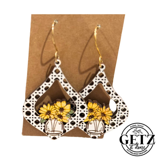Teardrop-shaped earrings with a leopard print and a transparent design. Each features a vase with yellow flowers. They hang from gold hooks. Positioned on a brown backing card with a GETZ it done, Aledo, Texas logo in the bottom right.