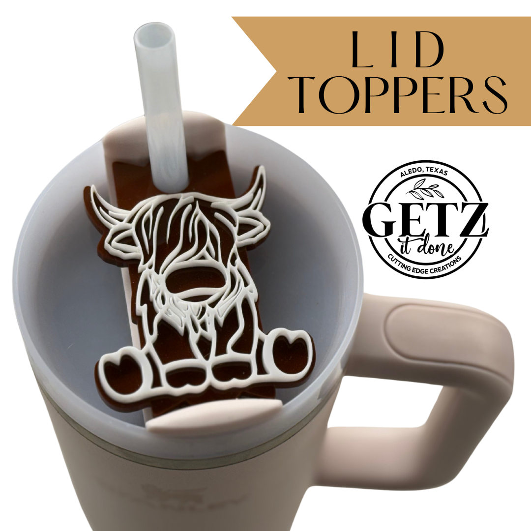 A white tumbler with a handle features a unique lid stopper shaped like a Highland cow, placed across the lid with a straw passing through it. The text Lid Toppers and Getz it Done with a logo for Aledo, Texas are displayed at the top right.