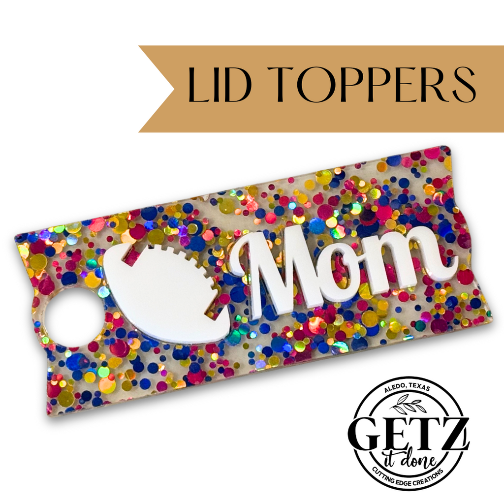 A colorful lid topper with a glittery design featuring multicolored confetti dots. The word Mom is prominently displayed alongside a football shape. The text LID TOPPERS appears at the top on a gold banner. The logo at the bottom reads GETZ it done, Aledo, Texas, Cutting Edge Creations.