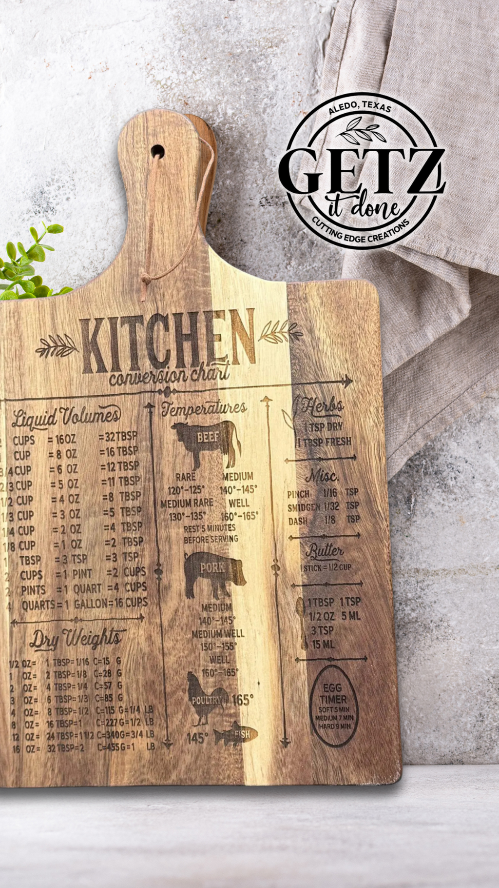 A wooden cutting board with engraved kitchen conversion charts for liquid volumes, temperatures, dry weights, meats, and eggs. It includes cups to ounces, teaspoons to tablespoons, and various cooking temperatures. A linen cloth is folded nearby, with a Getz It Done logo stamped above.