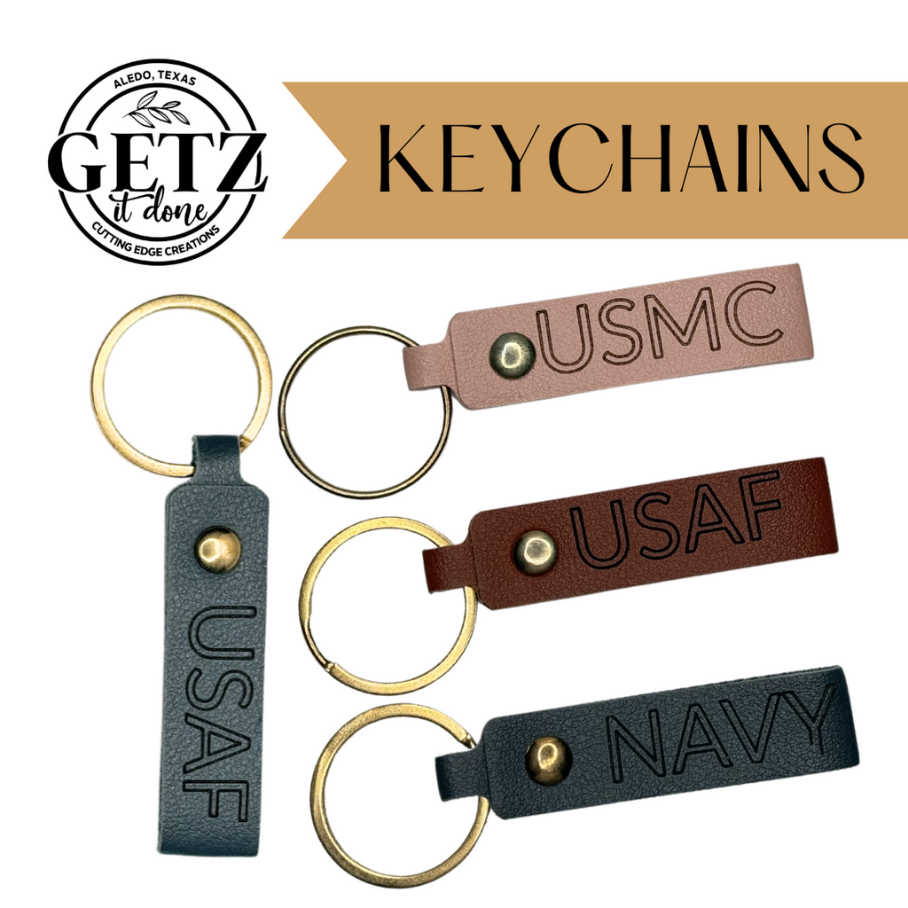 Image of three leather keychains with engraved military abbreviations: USMC on a light brown leather, USAF on a dark brown leather, and NAVY on a gray leather. They have gold metal rings. A circular logo at the top left reads Getz It Done, Aledo, Texas, Cutting Edge Creations.