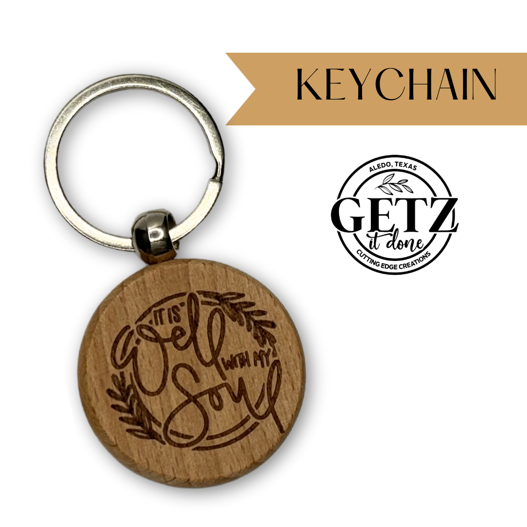Round wooden keychain with the words It is well with my soul engraved in a cursive font, surrounded by a leaf design. The top right has a beige banner with “KEYCHAIN” written on it. To the right, theres a logo with “GETZ It Done,” “Aledo, Texas,” and “Cutting Edge Creations.”.