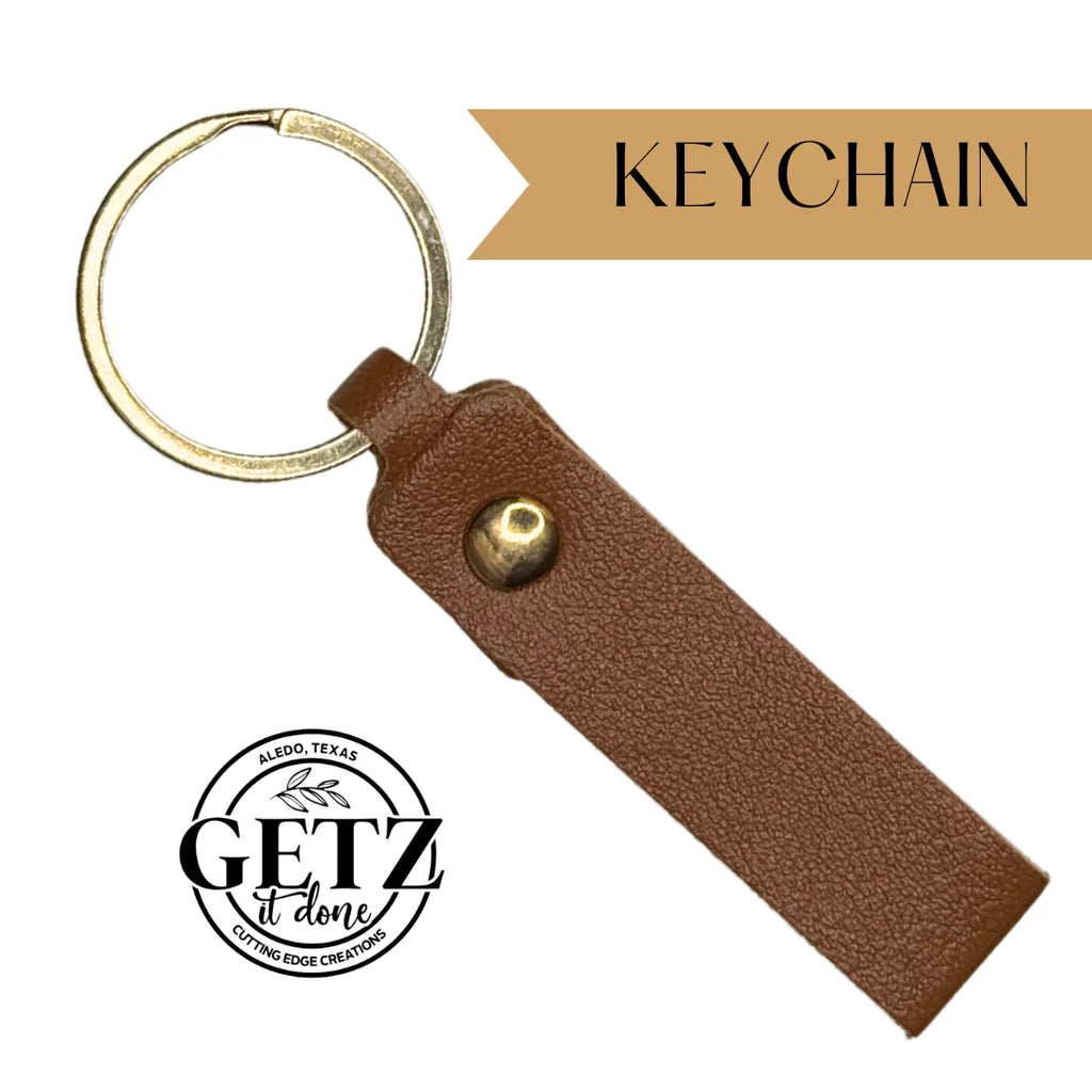 Brown leather keychain with a brass button and metal ring, displayed against a white background. Keychain is written in a tan banner at the top right. Bottom left features a circular logo with text Aledo, Texas and GETZ it done Cutting Edge Creations in black.