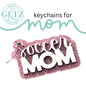 A sparkly pink keychain with the words Soccer MOM in bold white and black letters. Above it, the text keychains for mom is written in black and teal. The top left corner features the circular logo GETZ it done with Aledo, Texas and Cutting Edge Creations written within it.
