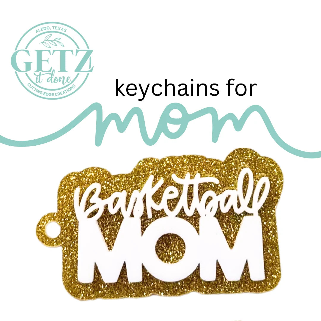 A glittery gold keychain with the words Basketball MOM in white letters. Above, the text reads keychains for mom in a mix of black and teal fonts. The top left corner features a logo with GETZ it done and Aledo, Texas Cutting Edge Creations.