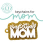 A glittery gold keychain with the words Basketball MOM in white letters. Above, the text reads keychains for mom in a mix of black and teal fonts. The top left corner features a logo with GETZ it done and Aledo, Texas Cutting Edge Creations.