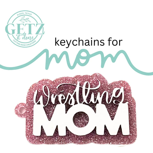 A glittery pink keychain with the words Wrestling MOM in white, bold and cursive letters. Above, text reads keychains for mom with a stylized line. The logo GETZ it done is in the upper left corner, noting Albedo, Texas, and Cutting Edge Creations.