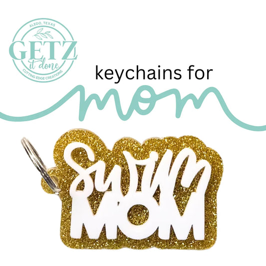 A gold glittery keychain with Swim Mom written in white letters. Above, the text keychains for mom is displayed in a mix of black and teal cursive. The logo GETZ it done with Aledo, Texas is in the top left corner.