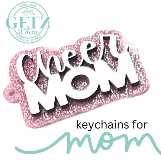 A pink glittery keychain with the words Cheer MOM in white letters. The bottom left features a green circular logo with GETZ it done and Aledo, Texas. The text keychains for mom is written in black and green below the keychain.