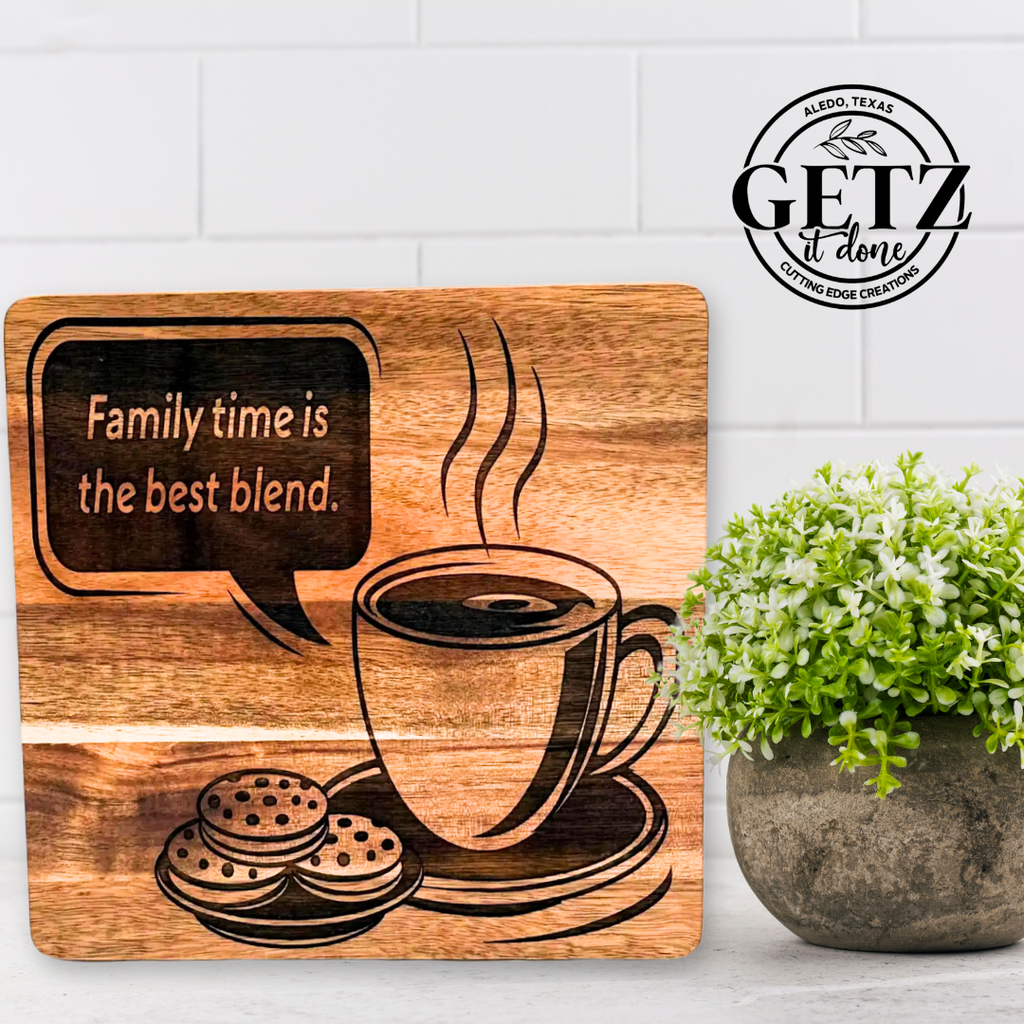 A wooden plaque sits on a countertop against a tiled backsplash. It features an illustration of a steaming coffee cup and cookies, with the text Family time is the best blend. Next to it is a potted plant with small, round green leaves. The logo GETZ it done is in the top right corner.