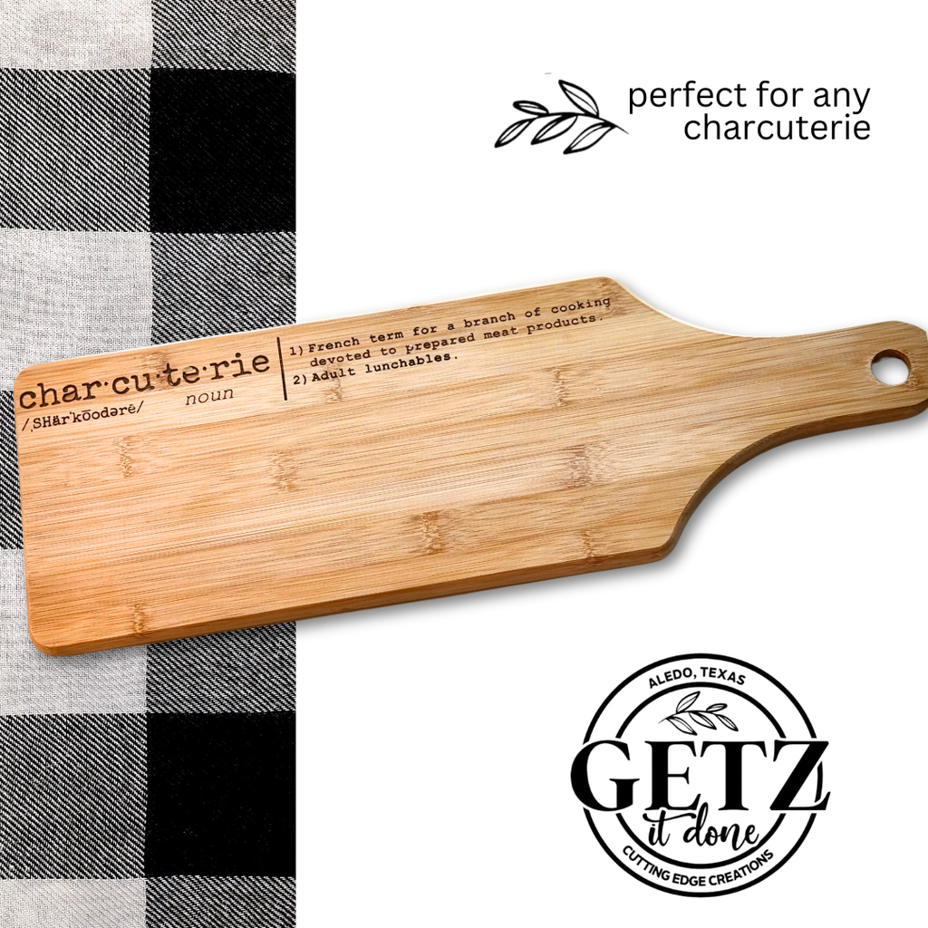 A wooden charcuterie board engraved with a definition of charcuterie and a small handle with a hole. It rests on a black and white checkered cloth. Text reads perfect for any charcuterie and displays a logo with Getz it done and Cutting Edge Creations, Aledo, Texas.