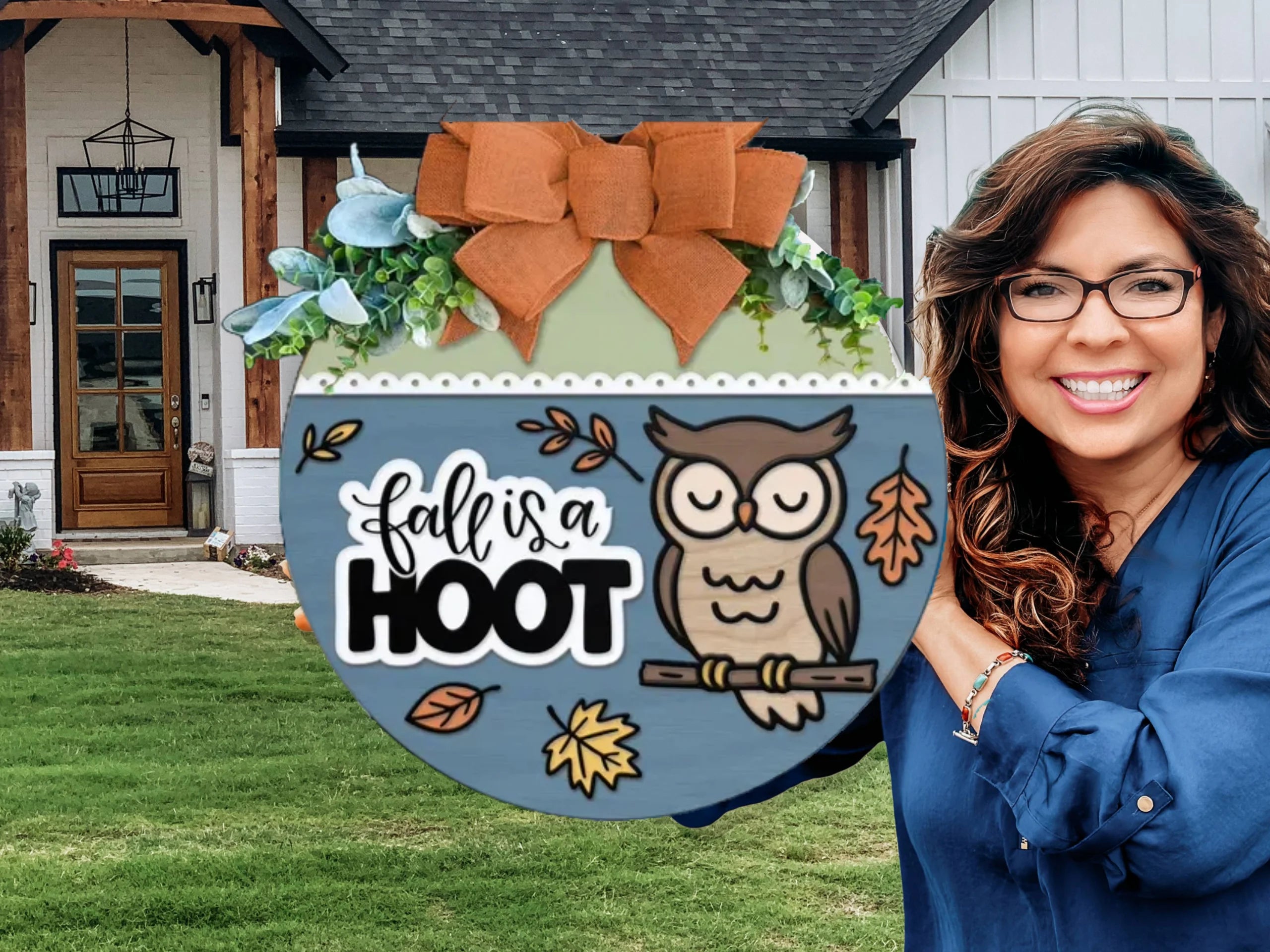 A smiling woman stands in front of a house holding a round fall-themed sign decorated with an owl, leaves, and the words fall is a HOOT, topped with a large orange bow and greenery.
