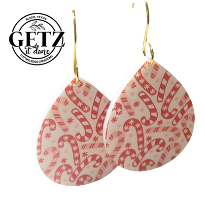 Teardrop-shaped earrings with a red and white candy cane pattern, featuring small snowflakes. The earrings have gold hooks. The background is white, and the logo in the corner reads GETZ it done, Aledo, Texas, Cutting Edge Creations.
