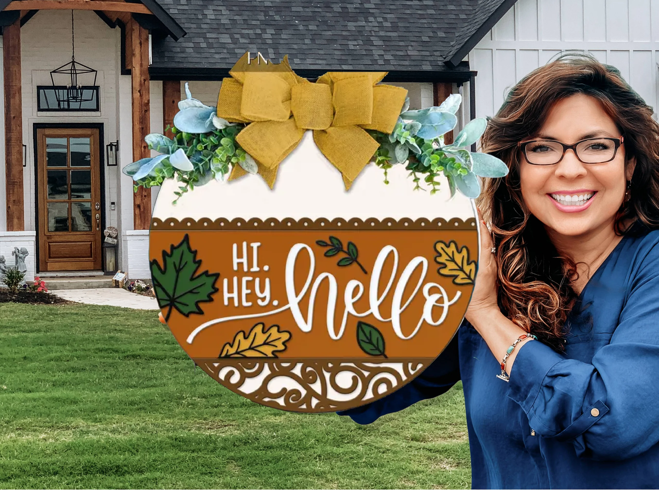 A smiling woman in glasses holds a round autumn-themed sign that says Hi. Hey. Hello in front of a modern house, with green grass and a wooden front porch visible in the background.