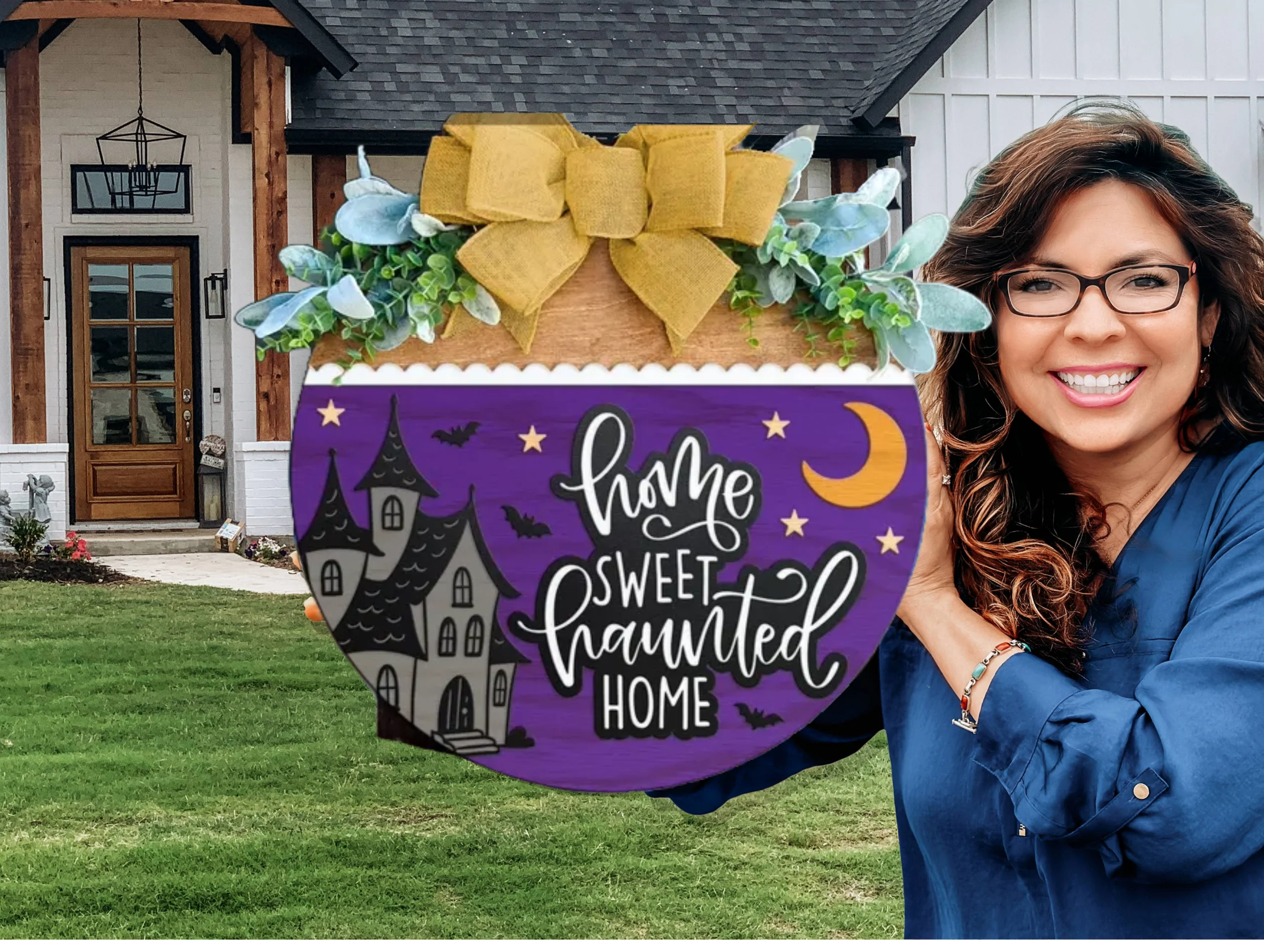A smiling woman stands outside a house, holding a round sign decorated with greenery and a large yellow bow. The sign reads, Home Sweet Haunted Home with a spooky house, bats, moon, and stars on a purple background.