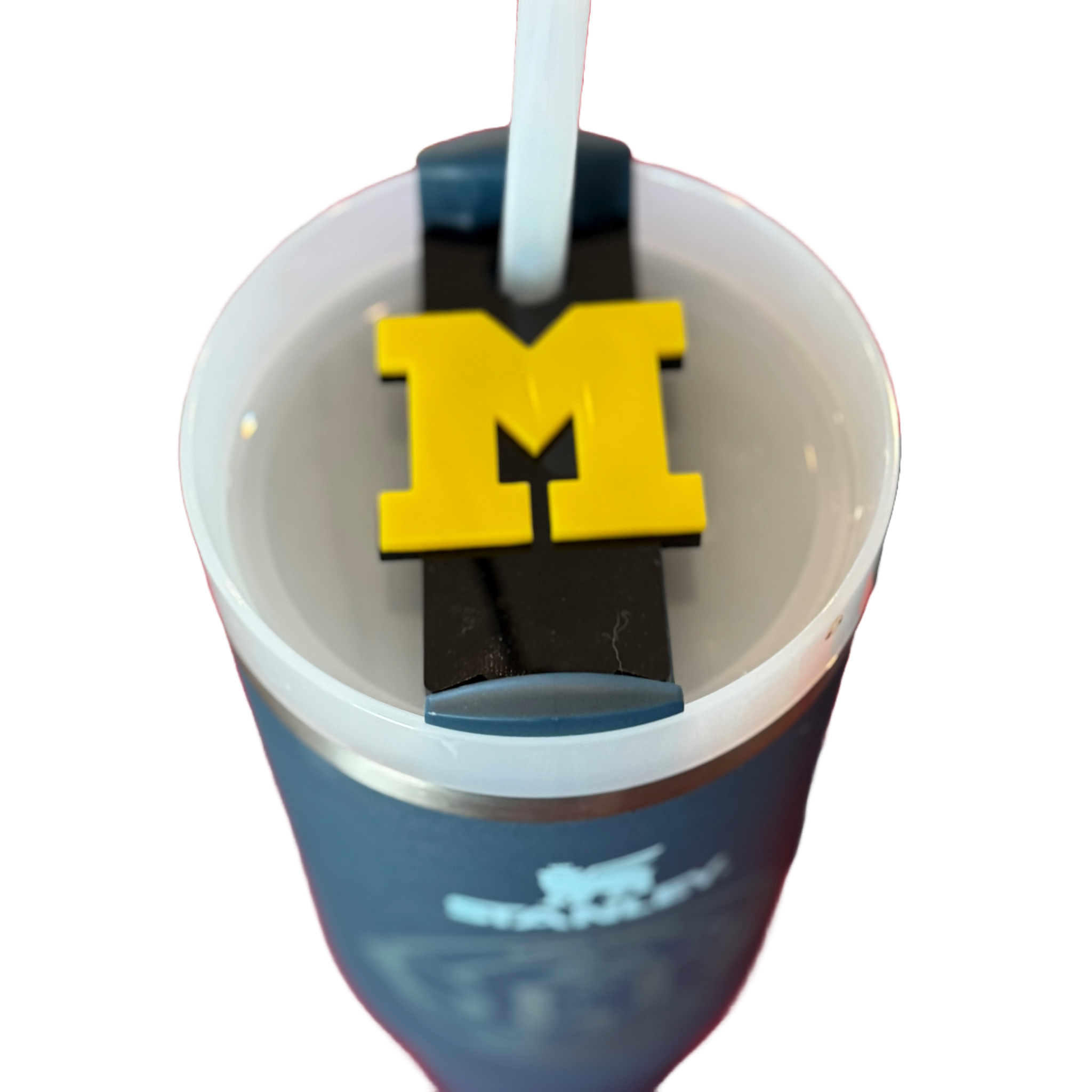 A blue cup with a lid features a straw passing through the center. On the lid, theres a clip with a large yellow M symbol. The clip appears to secure the straw in place. The cup has a partial blurred logo or design on the side.