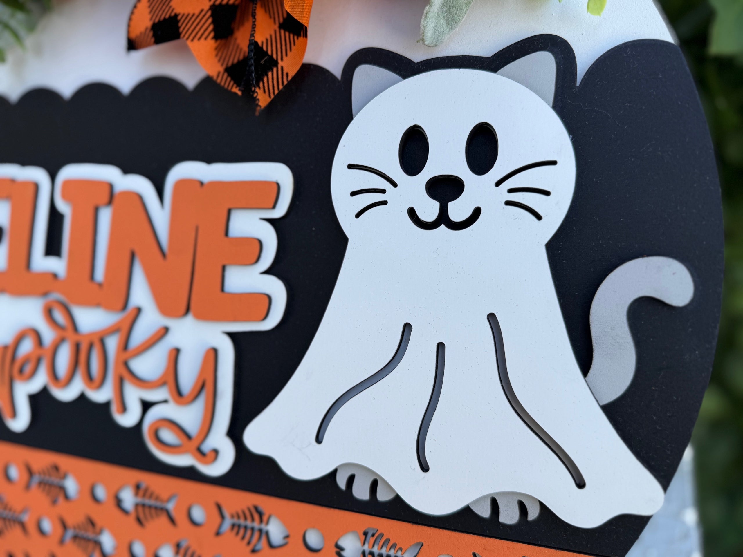 A cartoon cat wearing a ghost costume is part of a Halloween-themed decoration with orange, white, and black colors and the word spooky visible in the background.
