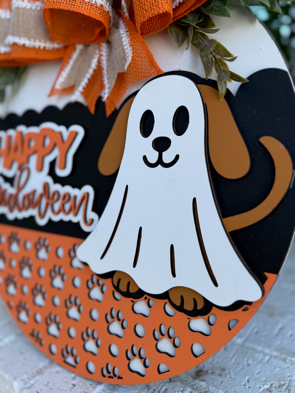 A Halloween decoration shows a cartoon dog wearing a ghost costume with visible ears, tail, and paws. Happy Halloween is written next to the dog, and the background features orange paw prints.