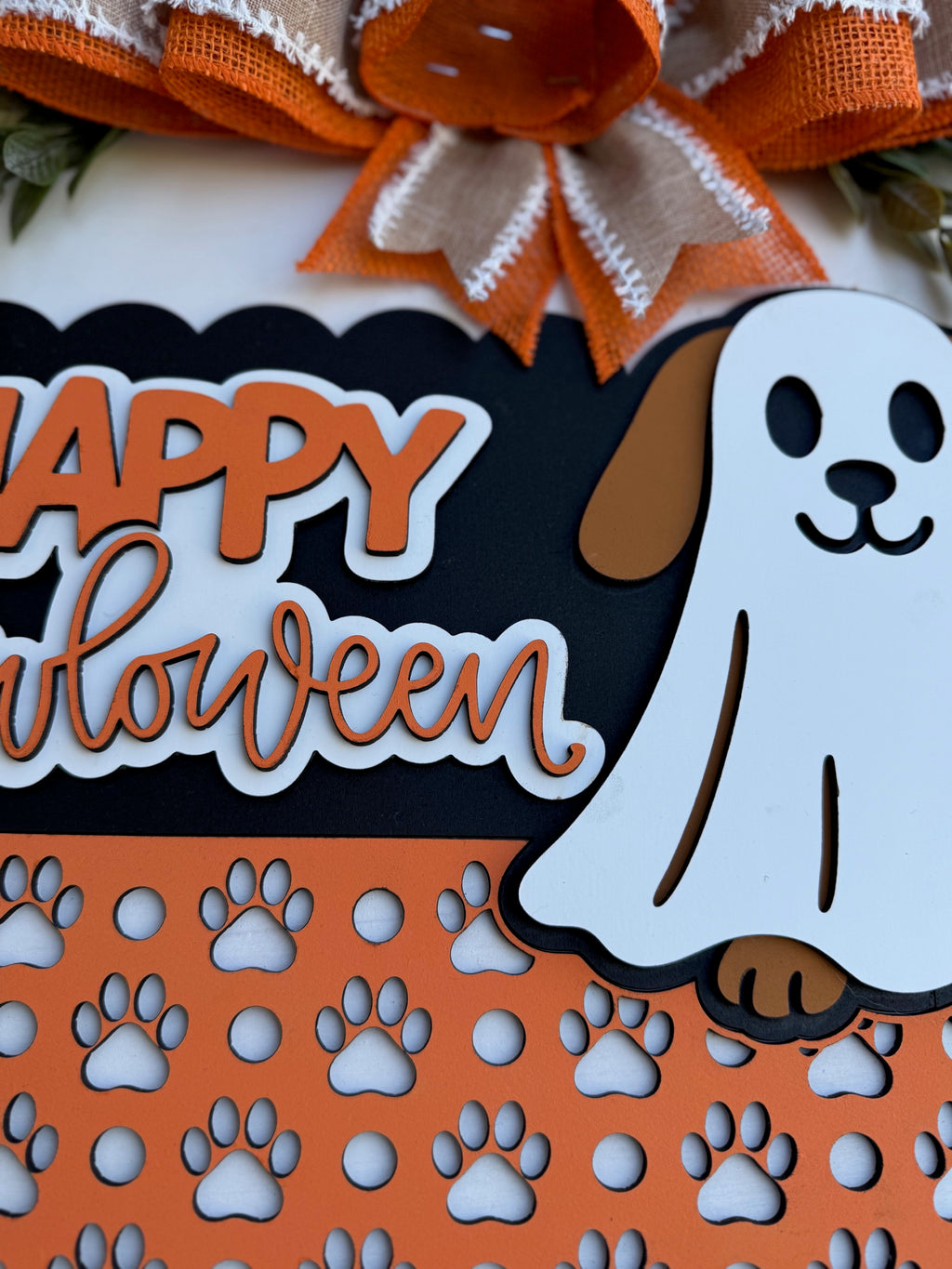 A Halloween-themed sign with a cartoon dog dressed as a ghost, orange and black colors, paw prints, and the text “Happy Halloween” above an orange and burlap ribbon bow.