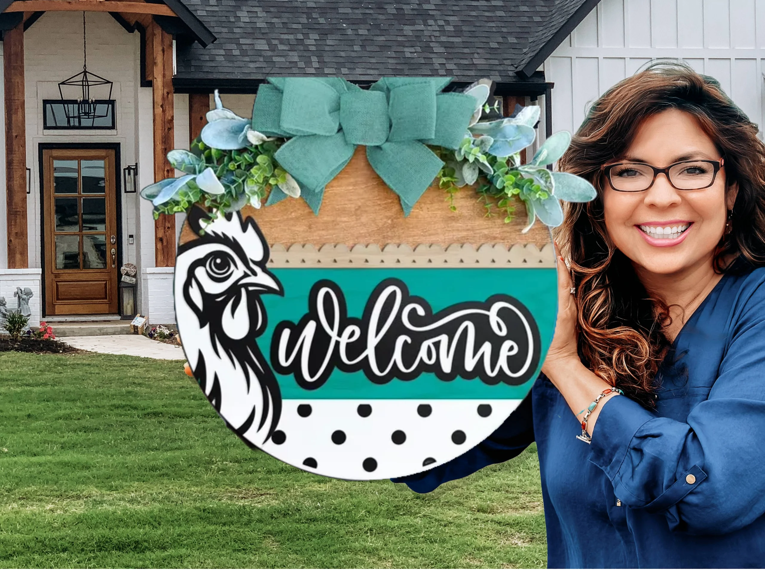 A smiling woman with long brown hair and glasses holds a colorful round Welcome sign with a rooster illustration and a green bow, standing in front of a modern farmhouse-style home.