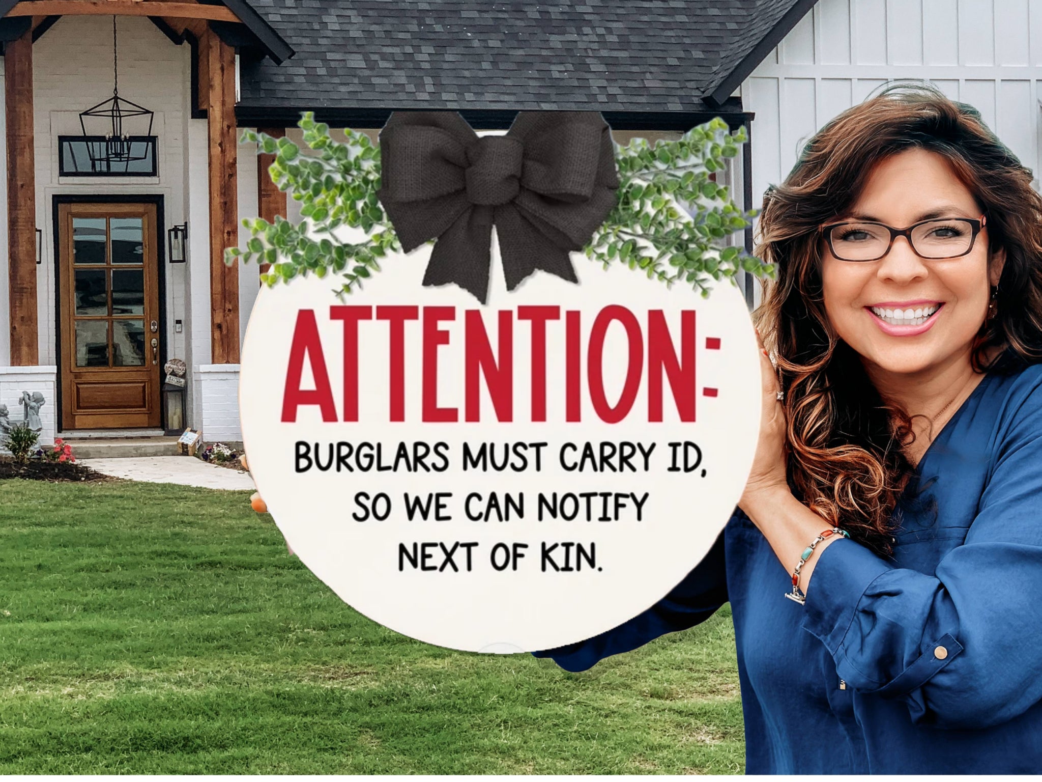 A smiling woman stands outside a house, holding a round sign that reads: ATTENTION: BURGLARS MUST CARRY ID, SO WE CAN NOTIFY NEXT OF KIN. The sign is decorated with greenery and a black bow at the top.