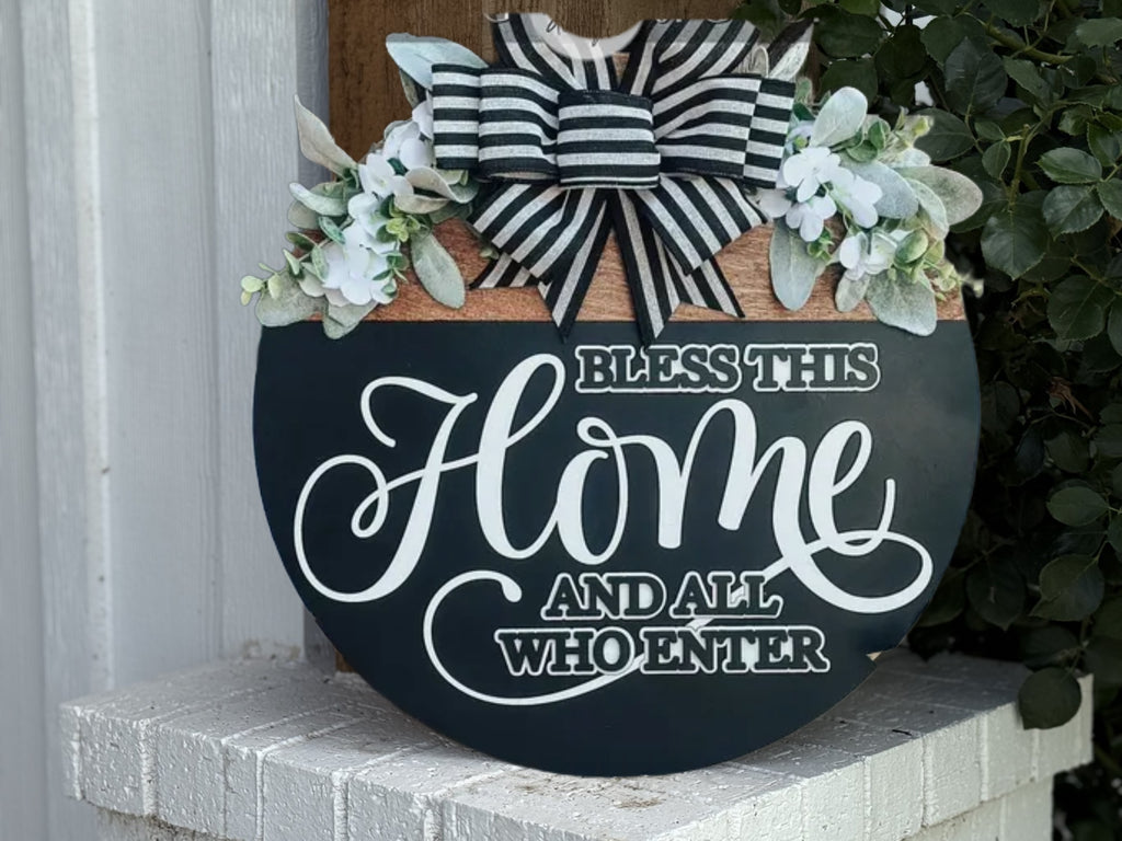 A round wooden sign reading “Welcome to the Porch” in farmhouse style with a black and white bow and white flowers. This rustic porch decor features “Gather Chat Unwind” and leans against a white brick ledge outside.