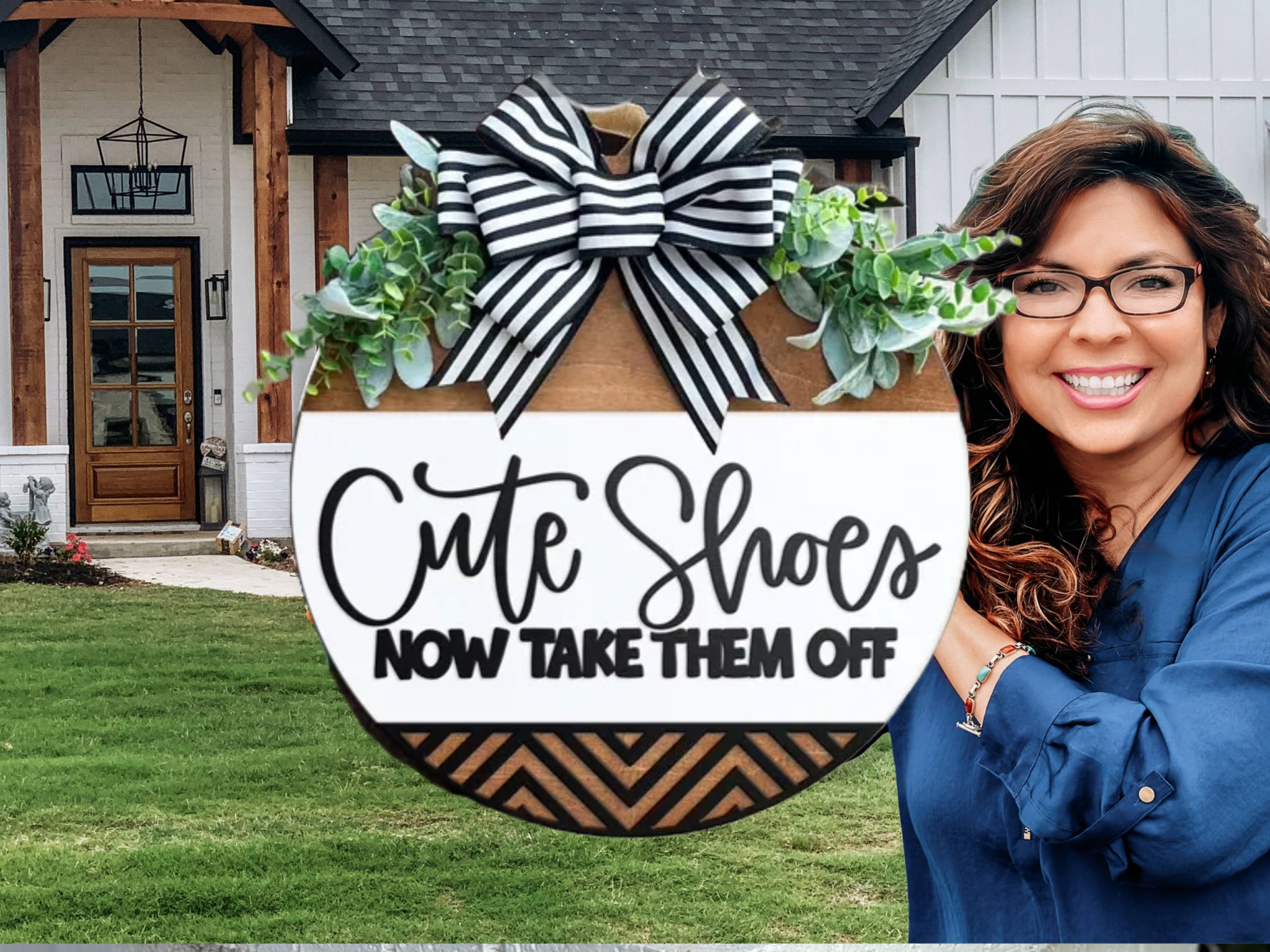 A smiling woman stands outside a house, holding a round decorative sign with greenery and a black-and-white striped bow. The sign reads, “Cute Shoes NOW TAKE THEM OFF.