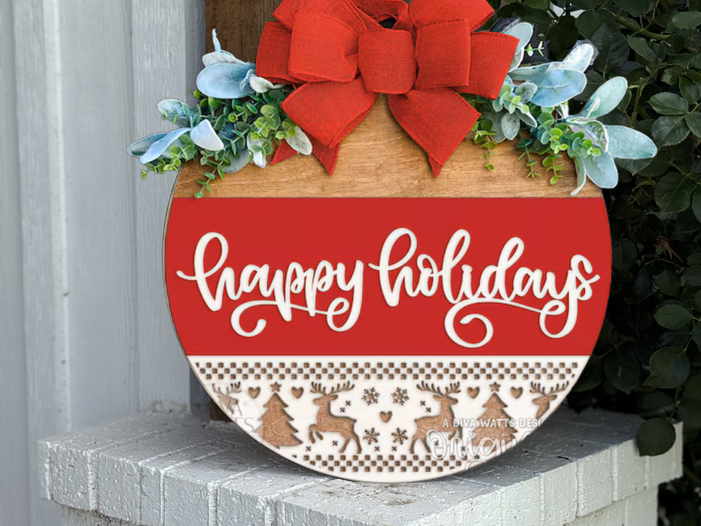 A round wooden holiday sign with a red bow, greenery, and the words happy holidays in white script. The bottom features a pattern of reindeer, trees, and snowflakes. The sign rests on a white brick surface.