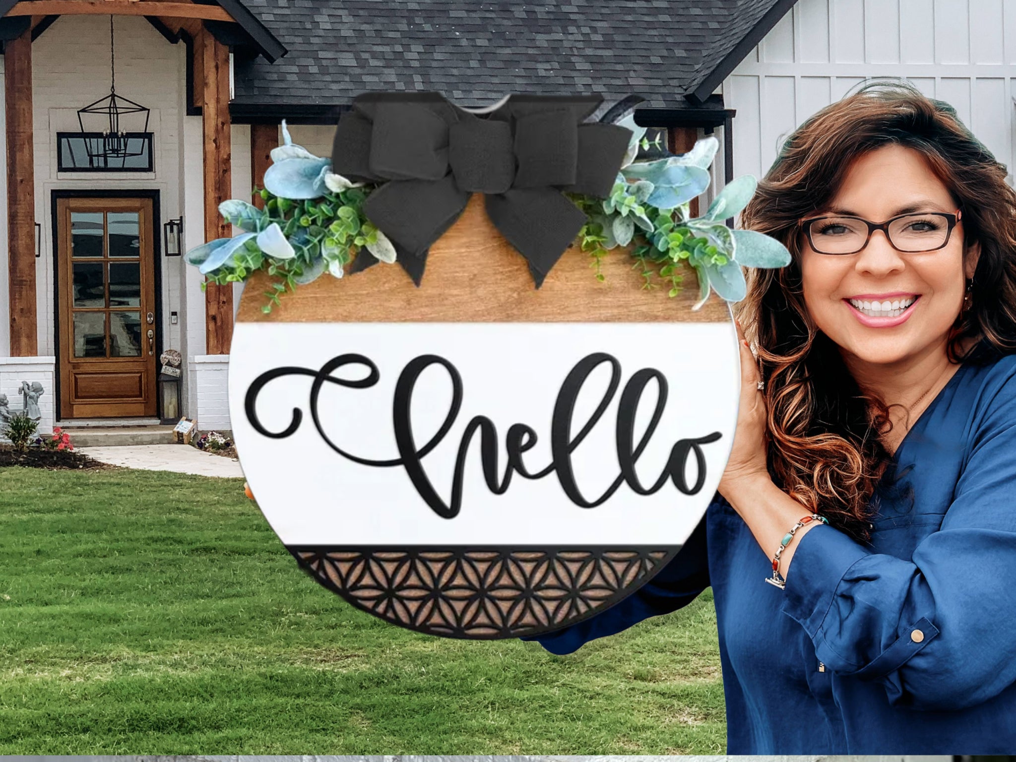 A smiling woman with long brown hair and glasses stands outside a house, holding a round wooden sign decorated with greenery and a black bow that says “Hello” in script.
