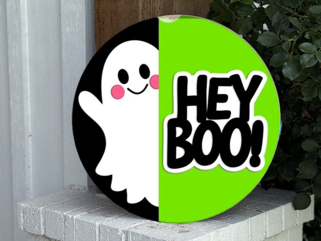 A round sign split in half, with a smiling cartoon ghost on the left and the words HEY BOO! in bold black letters on a bright green background on the right, leaning against a white brick surface and some greenery.