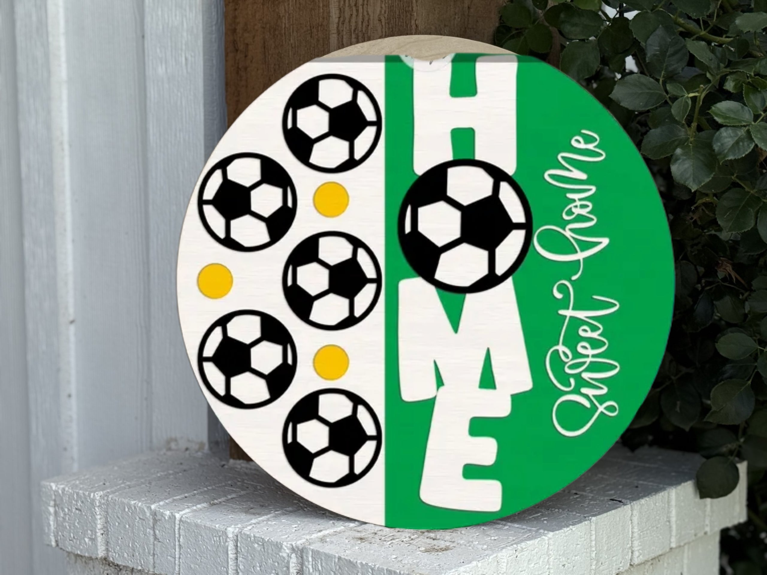 A round sign with soccer balls and yellow dots on the left and the word HOME on the right, with the letter O replaced by a soccer ball. The phrase Sweet Home is written in cursive along the side.