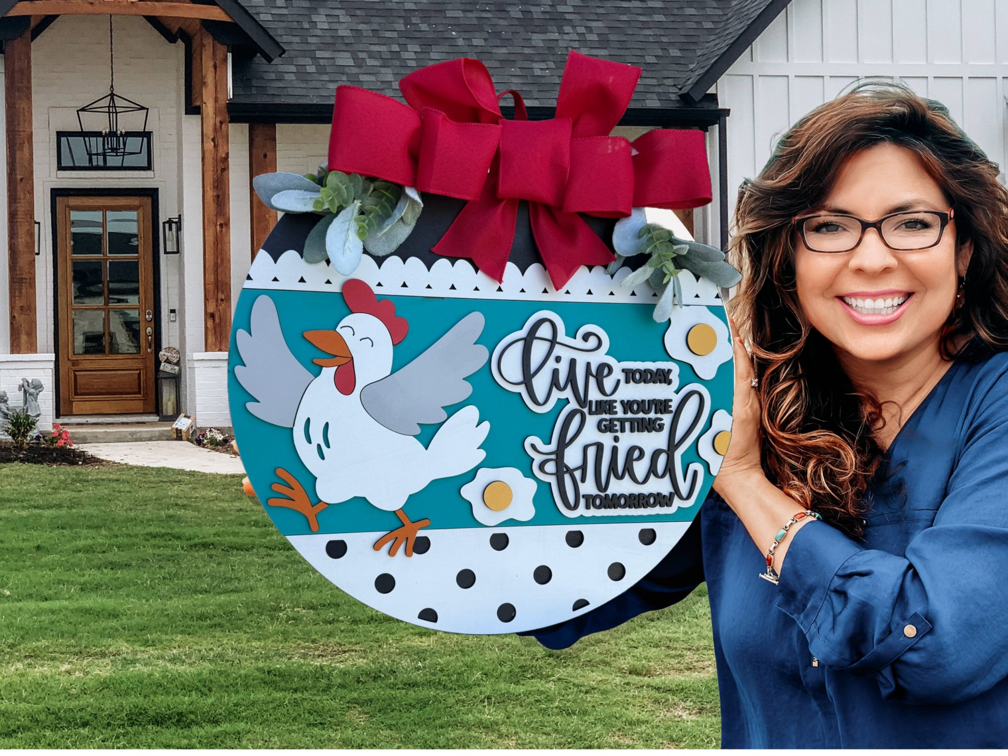 A round decorative sign with a cartoon chicken, eggs, and flowers, topped with red bows and greenery. The sign reads, Live today like youre getting fried tomorrow.