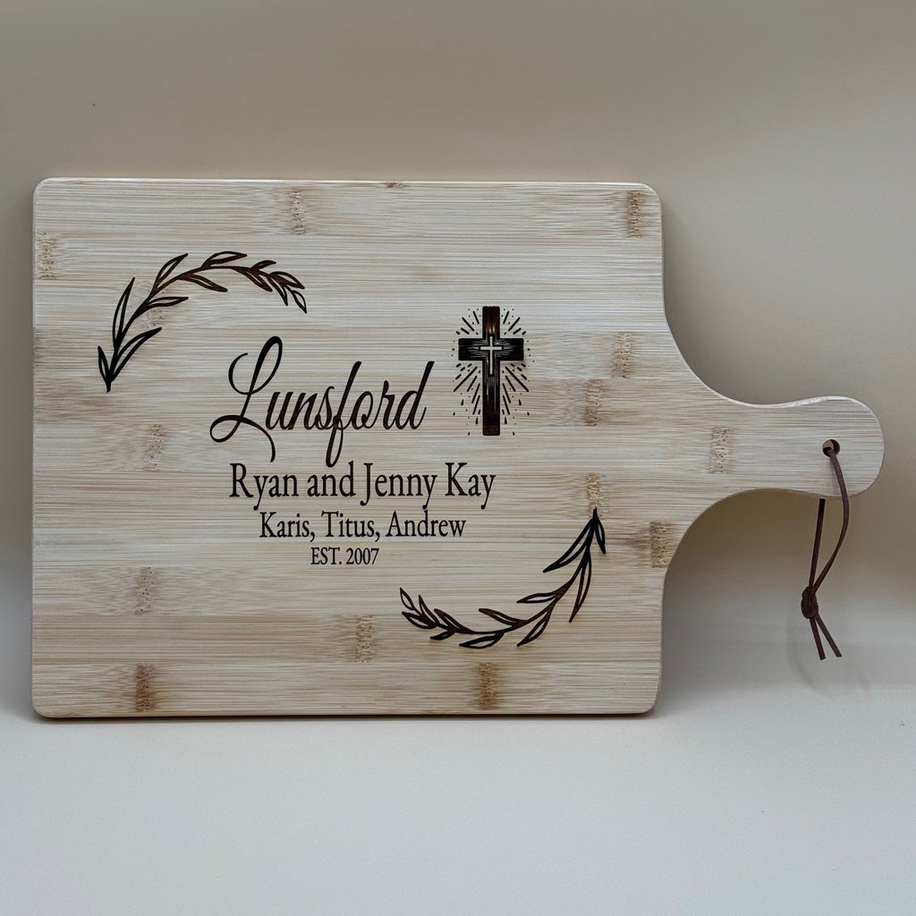 The personalized family information cutting board showcases Lunsford in elegant script. It includes cross and leaf designs on top corners, with a leather cord on the handle for easy display.