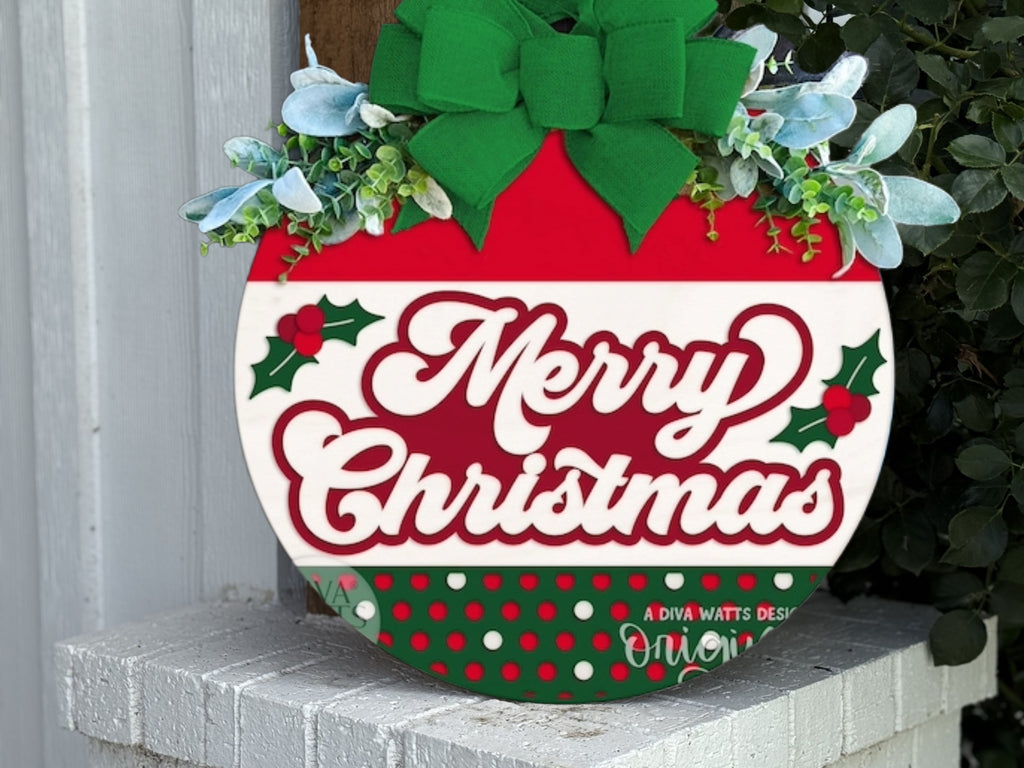 A round Christmas sign with a large green bow, holly decorations, and greenery reads Merry Christmas in festive red and white colors. The sign is placed on a white brick surface outdoors.