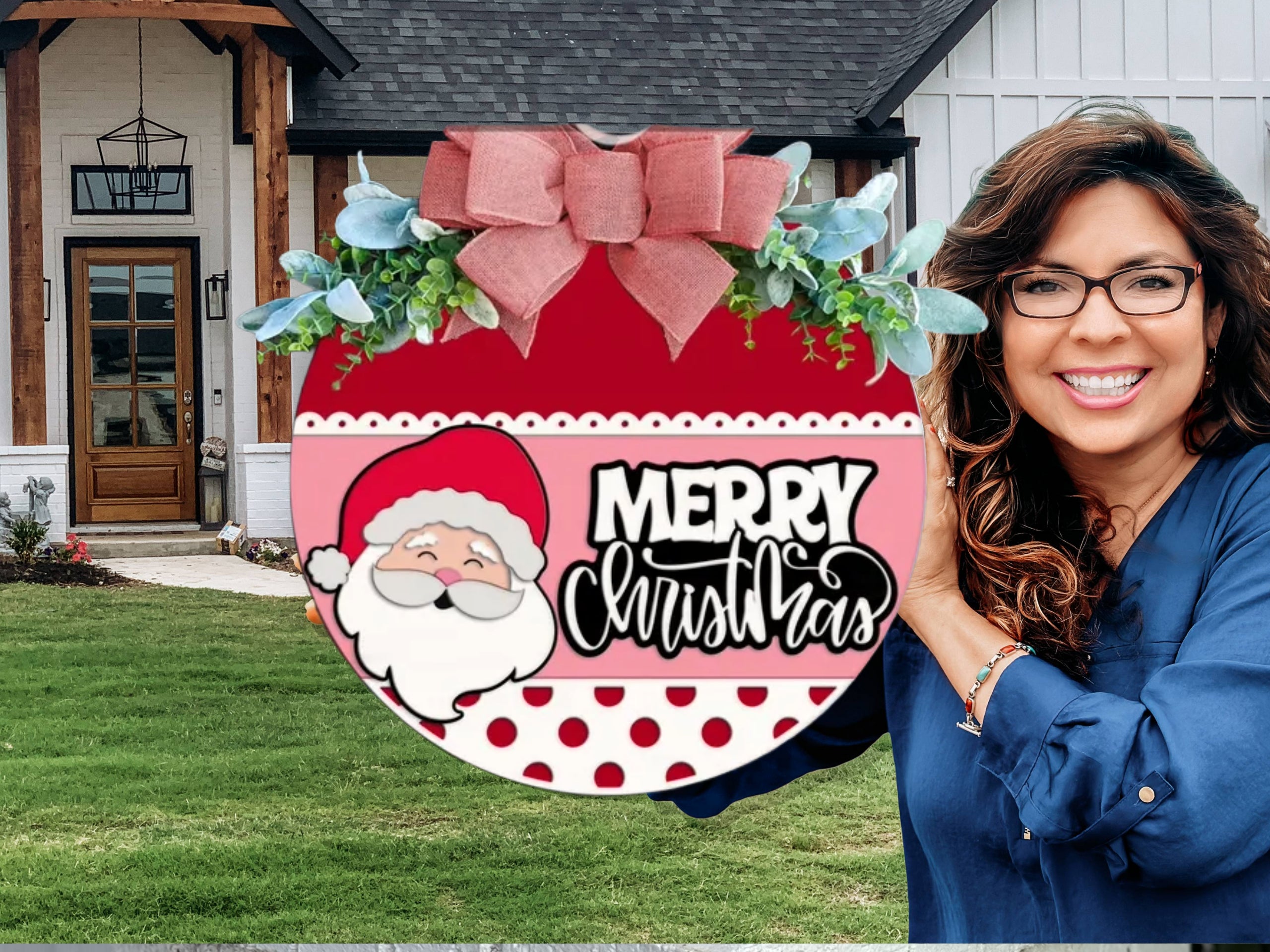 A smiling woman with glasses holds a round red Christmas sign decorated with Santa, polka dots, a bow, greenery, and the words Merry Christmas in front of a modern house with a green lawn.