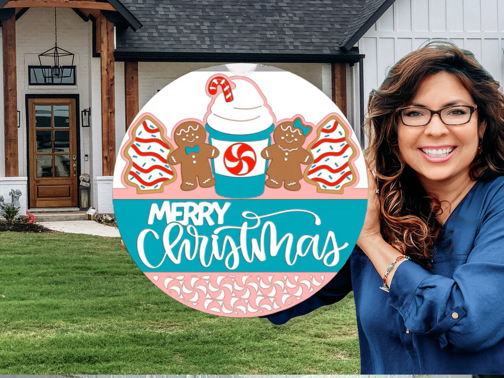 Round Christmas sign featuring two decorated gingerbread cookies, two frosted tree cookies, and a festive drink with a peppermint swirl and candy cane. The words Merry Christmas are written in white script.