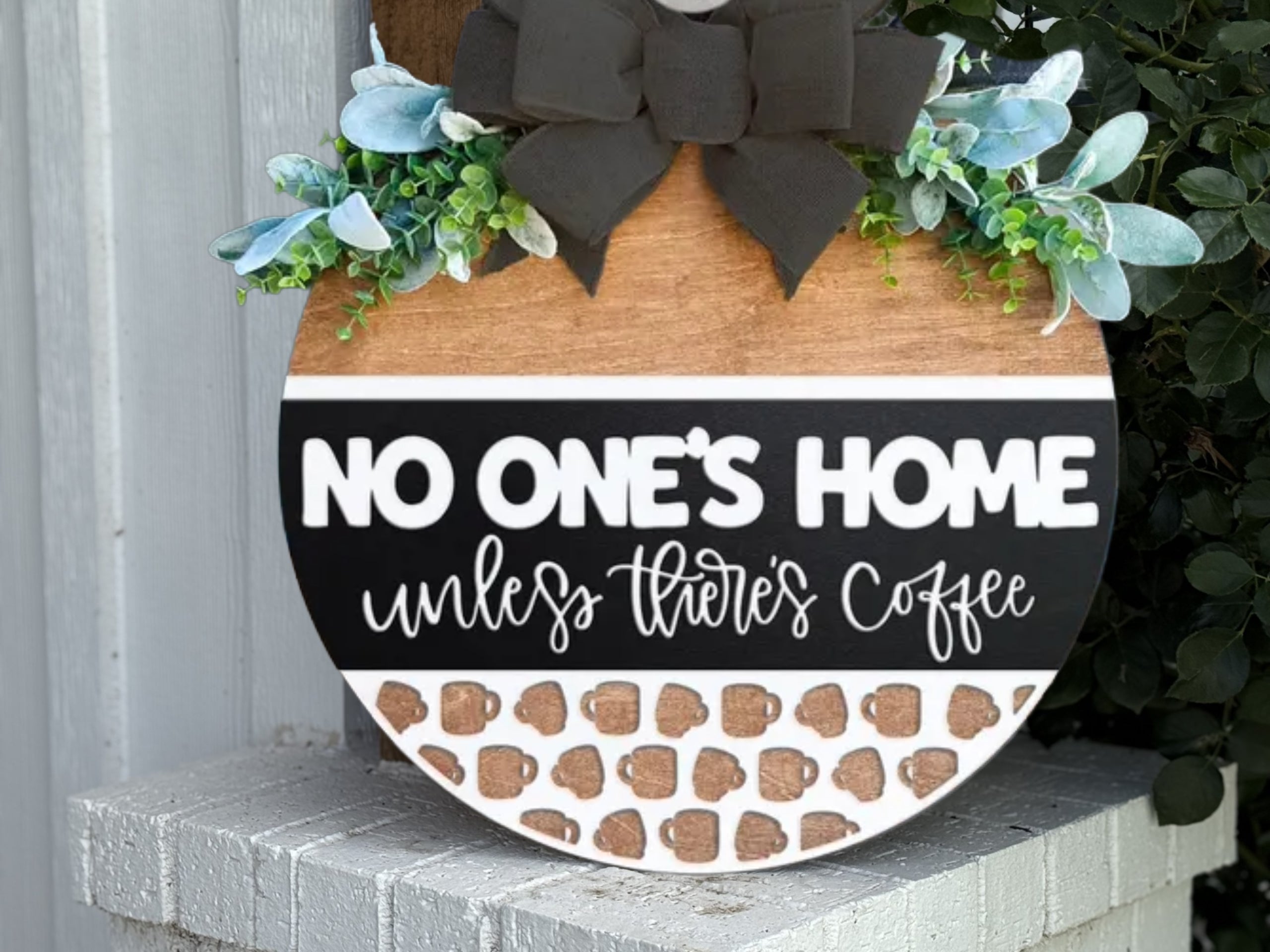 The "There's No Place Like Home Sign" is a rustic wooden door hanger with a black bow and greenery, perfect for farmhouse entryway or porch decor. Display it outdoors for a charming welcome to your home.