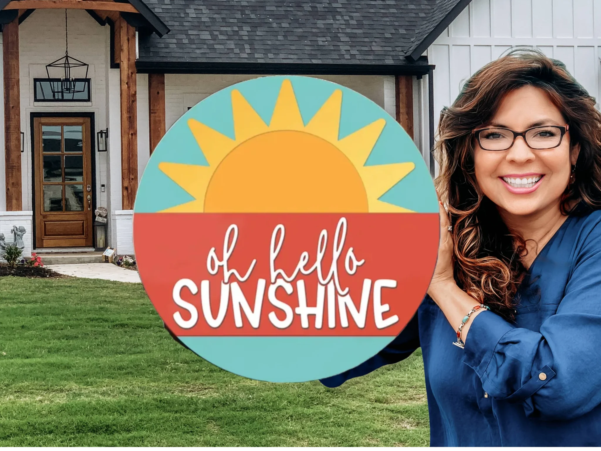 A smiling woman with long brown hair and glasses stands in front of a house, holding a round sign with a sun graphic and the words oh hello SUNSHINE written on it.