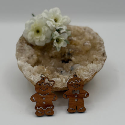Two wooden gingerbread ornaments, one with a bow and the other with a bow tie, stand in front of a geode. Behind them, white flowers rest on the geodes surface, adding a delicate touch to the scene.