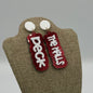 A pair of statement earrings with red glittery backgrounds. Each earring features white text; one reads Deck and the other The Halls. The earrings are displayed on a burlap-textured stand, against a neutral gray background.