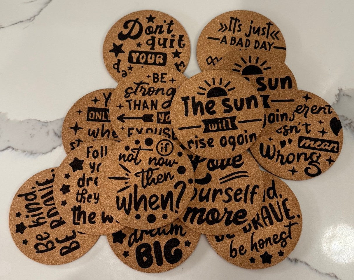 The Motivational Cork Coasters - Set of 4 inspires with phrases like The sun will rise again and Be kind, be brave, beautifully arranged in an overlapping pattern on a white marble surface while protecting your surfaces.