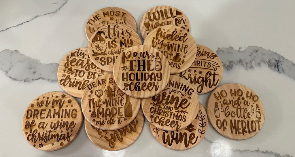 The Funny Wine Sayings: Set of 4 Round Wooden Coasters features humorous holiday-themed phrases like Pour the holiday cheer and Ho ho ho and a bottle of Merlot, neatly arranged in an overlapping circle on a marble surface.